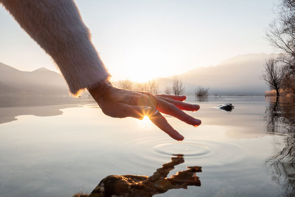 persons hand about to touch the water in a cool lake