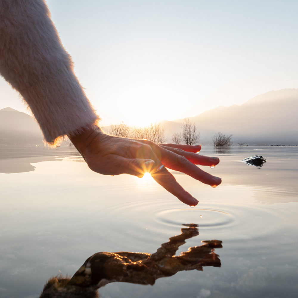 persons hand about to touch the water in a cool lake